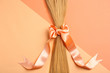Blond hair tied with ribbon on color background, top view