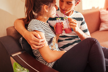 Couple in love drinking smoothie chilling on sofa in living room. Man and woman hugging enjoying drinks