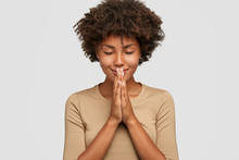 Meditation Concept. Beautiful Young Black Woman Stands In Meditative Pose, Enjoys Peaceful Atmosphere, Holds Hands In Praying Gesture, Isolated Over White Background, Has Sense Of Inner Peace