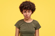 Dissatisfied woman frowns lips, has negative facial expression, dressed in casual clothes, poses against yellow background. Confused discontent African American girl has doubts, doesnt like something