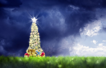 Wall Mural - conceptual decorated shiny christmas tree on green landscape over cloudy sky