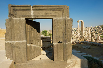 Ancient carved Basalt Door at the Citadel of Amman with ruined columns and the city at the background in Amman, Jordan.