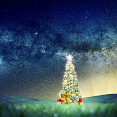 Wall Mural - Conceptual image of Decorated Christmas tree on green landscape over night sky with stars and galaxies.