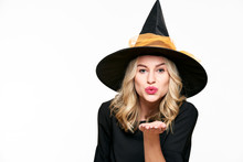 Sensual Halloween Witch Studio Portrait. Attractive Young Woman Dressed In Witch Halloween Costume Isolated Over White Background Blowing A Kiss Towards Camera.