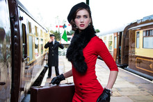 Vintage Attractive Female Wearing Red Dress And Black Beret With Suitcases On Platform Of Train Station