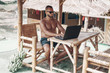 © Semachkovsky  - young businessman in sunglasses blue shirt and shorts working with laptop on the beach