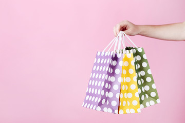 Wall Mural - Female hand holding colorful shopping bags on pink background