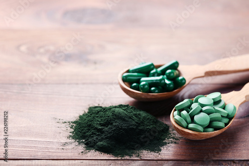 Fotografia Spirulina powder and tablets in spoons on brown wooden table