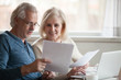 © fizkes - Happy old middle aged couple holding reading good news in document, smiling senior mature family excited by mail letter, checking paying domestic bills online on laptop, discussing budget planning