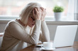 © fizkes - Upset depressed mature middle aged woman in panic holding head in hands in front of laptop frustrated by bad news, online problem or being fired by email feeling desperate shocked exhausted concept