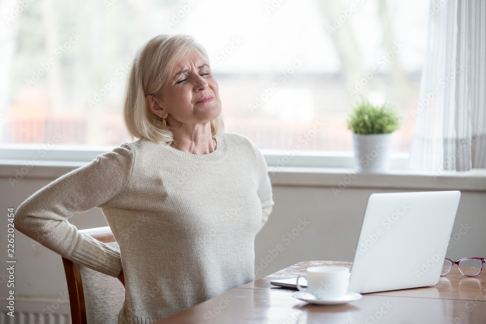 Upset mature middle aged woman feels back pain massaging aching muscles, sad senior older lady suffers from low-back lumbar pain sitting in incorrect sedentary posture, backache radiculitis concept - obrazy, fototapety, plakaty 