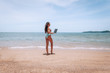 © Semachkovsky  - Young american woman in blue swimsuit working with laptop on empty beach. Concept of resting on morning sea and summer vacations, modern technology.