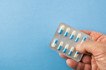 Hand holding blister pack of blue and white pills on blue background with copyspace