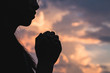 © Tinnakorn - Silhouette off   young woman praying for God's blessings with the power and power of the sacred On the background of sunrise. The concept of God and spirituality.