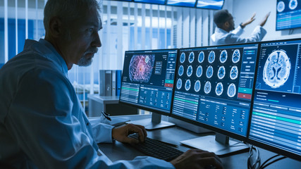 Over the Shoulder Shot of Senior Medical Scientist Working with CT Brain Scan Images on a Personal Computer in Laboratory. Neurologists in Research Center Work on Brain Tumor Cure.