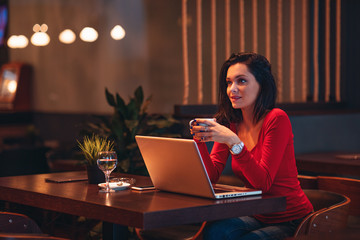 Beautiful young woman holding coffee in a cafe with a laptop on the table