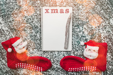 Empty Page Of Spiral Notebook And Christmas Red Stockings On A Snow Background. Flat Lay, Hightlights Effect