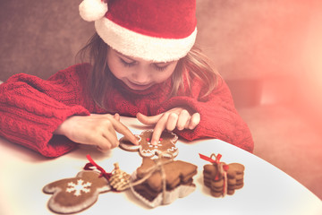 Little girl decorates gingerbread in Santa's red hat