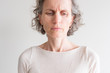 © Natalie Board - Close up head and shoulders view of middle aged woman with grey hair and cream top frowning and showing wrinkles (selective focus)