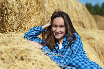 Poster - Natural frontal portrait of a smiling young woman standing leaning on a haystack