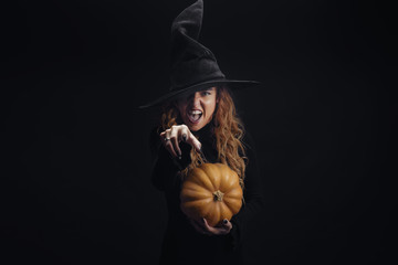 Halloween Witch with pumpkin. Pretty young woman in witch costume. Halloween decor. Copy space.