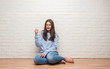 © Krakenimages.com - Young brunette woman sitting on the floor over white brick wall annoyed and frustrated shouting with anger, crazy and yelling with raised hand, anger concept