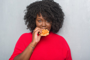 Poster - Young african american woman over grey grunge wall eating belgium waffle with a confident expression on smart face thinking serious