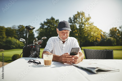 Fotografie, Obraz Senior man using a cellphone at his golf club restaurant