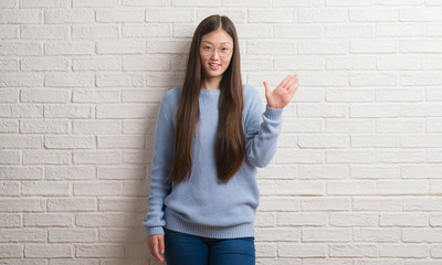 Young Chinise woman over white brick wall showing and pointing up with fingers number five while smiling confident and happy.