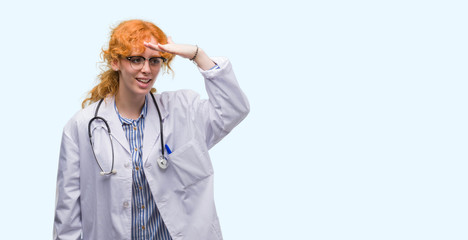 Poster - Young redhead woman wearing doctor uniform very happy and smiling looking far away with hand over head. Searching concept.