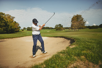 Senior man chipping out of a bunker while playing golf