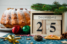 Traditional Fruitcake For Christmas Decorated With Powdered Sugar And Nuts, Raisins Next To Wooden Calendar With Date 25 December Delicioius Homemade Pastry. New Year And Christmas Celebration Concept