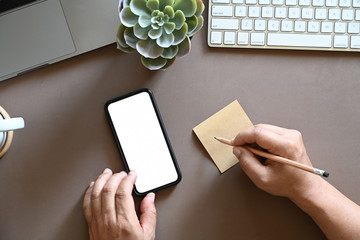 Top view shot of man writing sticky note and using mobile phone