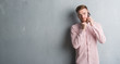 © Krakenimages.com - Young redhead man over grey grunge wall talking on the phone serious face thinking about question, very confused idea