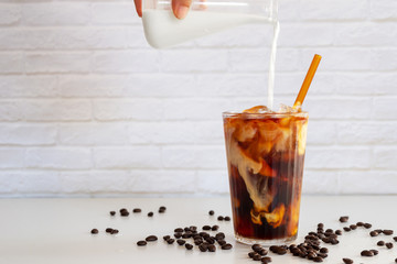 Wall Mural - Pouring milk into a glass of homemade cold brew coffee on white table