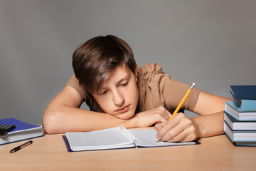 Wall Mural - Tired teenager boy doing homework against grey background