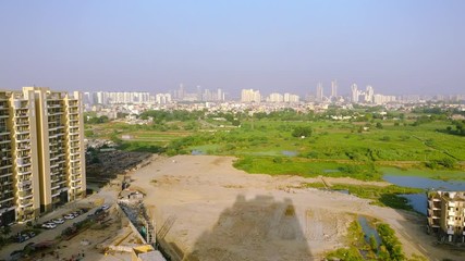 Wall Mural - Aerial pan from an under construction building to farms, lakes, and grassy farmlands in gurgaon. Showcases how new real estate projects are coming up and taking over the rural areas of gurgaon noida