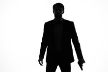Dark Silhouette Of A Man With A Gun In His Hand On A Light Background
