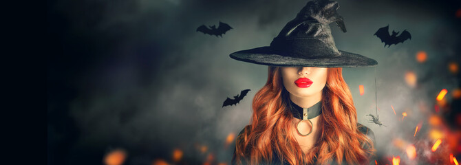 Halloween. Sexy witch portrait. Beautiful young woman in witches hat with long curly red hair over spooky dark magic forest background