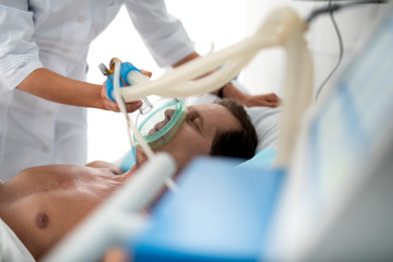 close up portrait of middle aged man with oxygen mask lying in bed. doctor hands using respiratory e