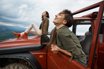 Wall Mural - Cheerful beautiful young woman enjoying her active weekend with her friend while traveling in the off-road car