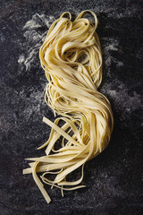 Variety of italian homemade raw uncooked pasta spaghetti and tagliatelle with semolina flour over black texture background. Flat lay, space