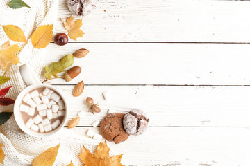 Autumn composition. Dark scarf, a cup of cocoa with marshmallows, autumn dry leaves on a white wooden table. Top view. Copy space