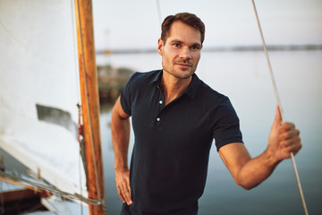 Young man standing by the rigging of his yacht