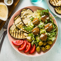 an appetizing dinner or lunch from a salad with tomatoes, grilled eggplants and legume falafel with sesame tahini dressing. Vegan healthy food for the whole family