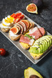 A set of avocado sandwiches, cherry tomatoes and eggs, figs, prochutto on a stone background