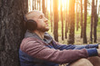 Man in headphones is sitting in a forest with his back to a tree. Concept of outdoor recreation and relaxation. Sounds of nature
