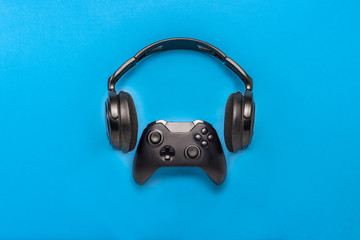 Wall Mural - Black headphones and a gamepad on blue background. Concept of the game on the console or computer. Rest after work. Cybersport. Flat lay, top view