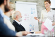 © pressmaster - Young economist in smart casual standing by whiteboard and talking to audience at seminar
