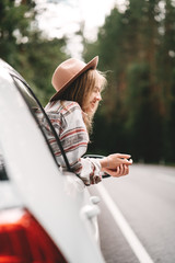 Wall Mural - Happy hipster girl traveling adventure vacations. Boho woman sitting in car looking from window on beautiful view in country road